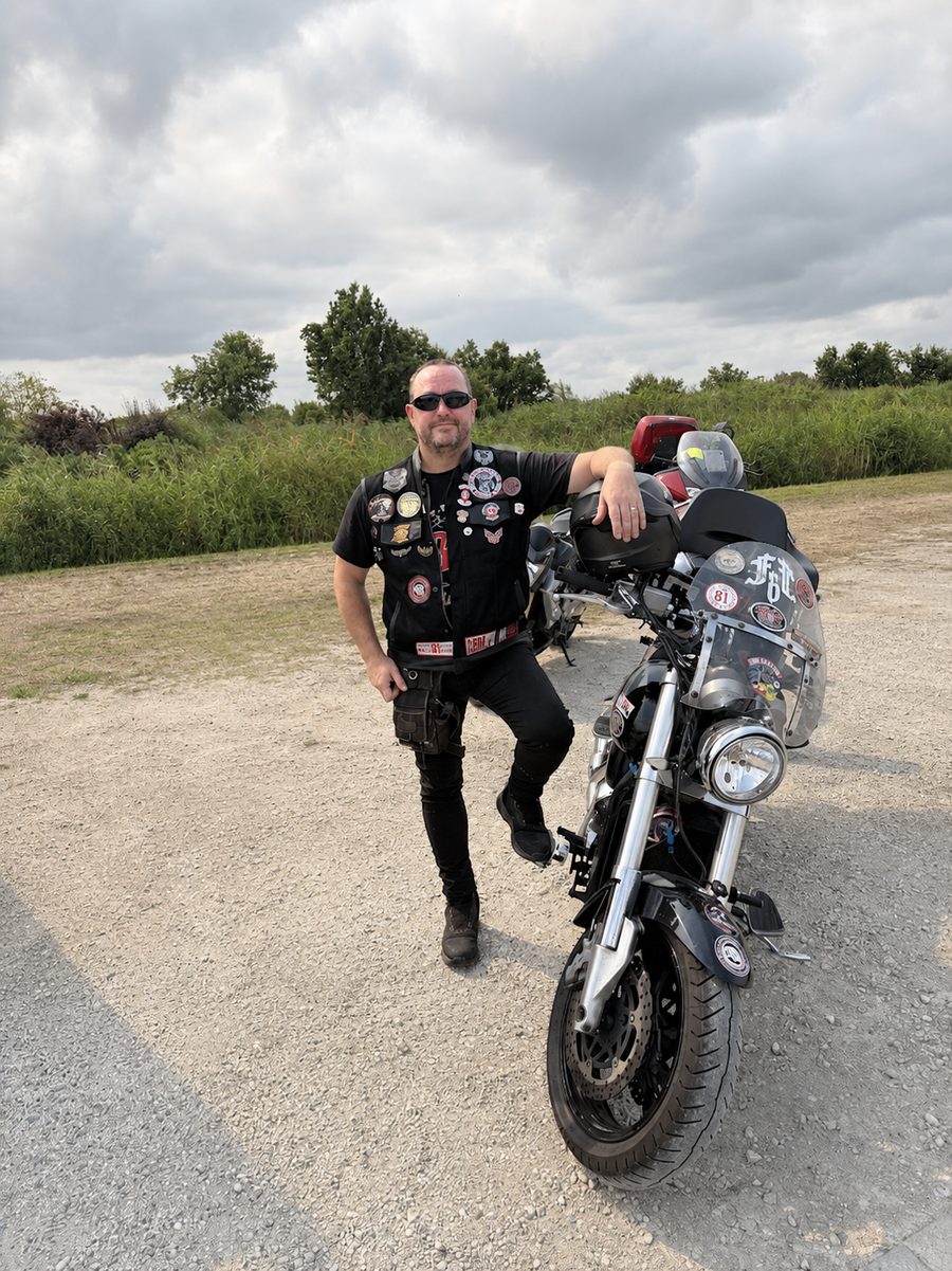 Christophe Bériol en tenue de biker, appuyé sur sa moto